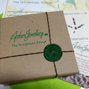 Pode incluir: Uma caixa de papel castanho com um selo de cera verde e corda. A caixa est&aacute; etiquetada "Archers' Jewellery The Wilderness Range".