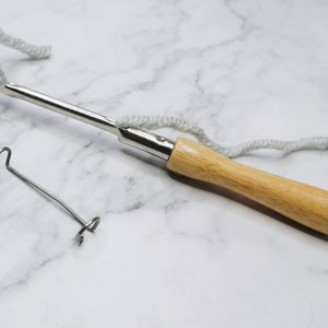 May include: A wooden handled yarn needle with a metal hook and a loop at the end of the handle. A separate metal loop is also pictured.