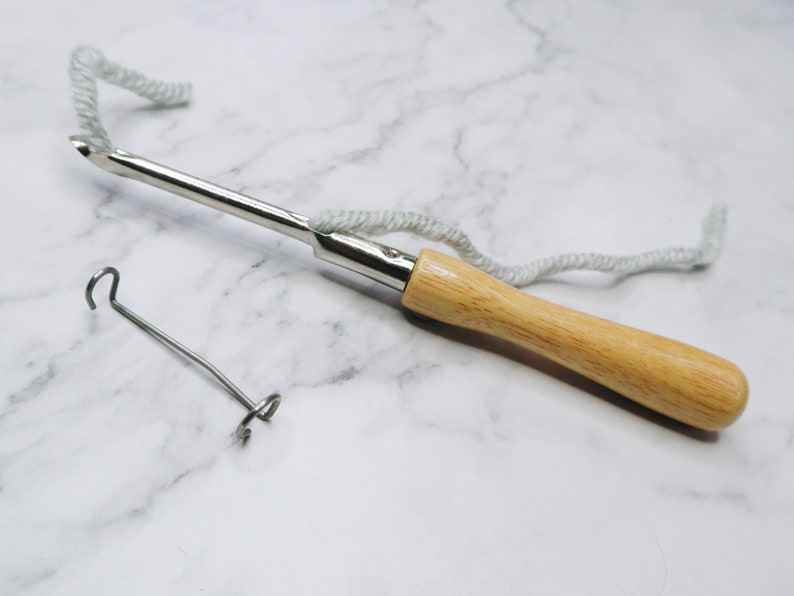 May include: A wooden handled yarn needle with a metal hook and a loop at the end of the handle. A separate metal loop is also pictured.