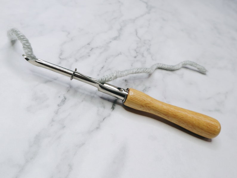 May include: A wooden handled yarn needle with a metal hook and a loop at the end of the handle. A length of white yarn is threaded through the needle.