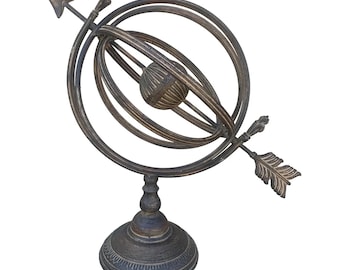Puede incluir: Un globo terráqueo decorativo de metal con una flecha apuntando hacia arriba. El globo está sobre un soporte con una base circular. El globo y el soporte están pintados de color marrón oscuro.