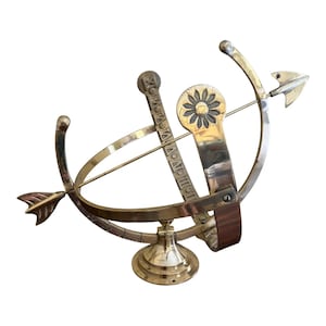 May include: A vintage brass armillary sphere with a decorative arrow and floral accents. The sphere features a circular design with a base and a wooden accent. The brass has a polished finish.