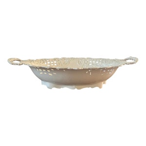 May include: White decorative bowl with a lacy design and two handles. The bowl is made of plastic and has a scalloped edge.