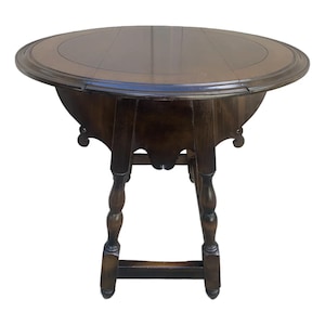 May include: A dark brown, round wooden table with a decorative edge. The table has a pedestal base with turned legs and a lower stretcher. The table is approximately 36 inches in diameter.
