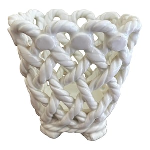 May include: A white ceramic vessel featuring a decorative openwork lattice design that mimics the appearance of twisted rope. The structure is cylindrical with a flared top rim and a solid base, creating a basket-like appearance with uniform gaps.