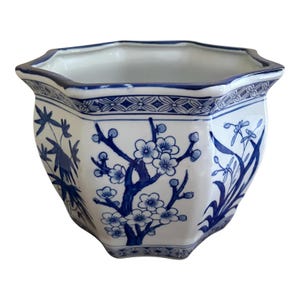 May include: An octagonal white and blue ceramic planter. The planter is decorated with blue floral and botanical patterns, including flowering branches and stylized leaves. The rim has a blue decorative border.