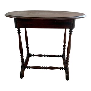 May include: A dark brown oval-shaped table with turned legs and a simple design. The table has a dark wood finish and a smooth surface.
