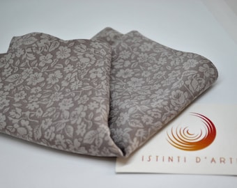 May include: A pair of folded fabric squares with a light brown background and a white floral pattern. The fabric is folded in half and the edges are visible. The fabric is lying on a white surface. The text "ISTINTI D'ARTE" is visible in the lower right corner of the image.