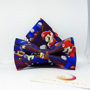 Puede incluir: Una pajarita azul y marrón con un patrón de personajes de Mario de la serie de videojuegos Super Mario. La pajarita está hecha de tela y tiene un patrón a rayas.