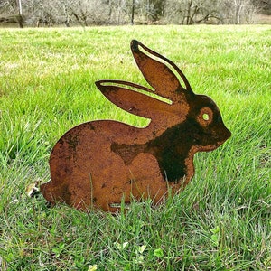 May include: A rusty metal rabbit silhouette garden decoration. The rabbit is sitting on a bed of green grass.