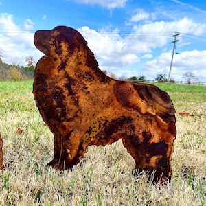 K&ouml;nnte beinhalten: Eine rostige Metallsilhouette eines Hundes, der auf einer braunen und gr&uuml;nen Wiese steht. Der Hund blickt nach links und hat einen langen Schwanz.