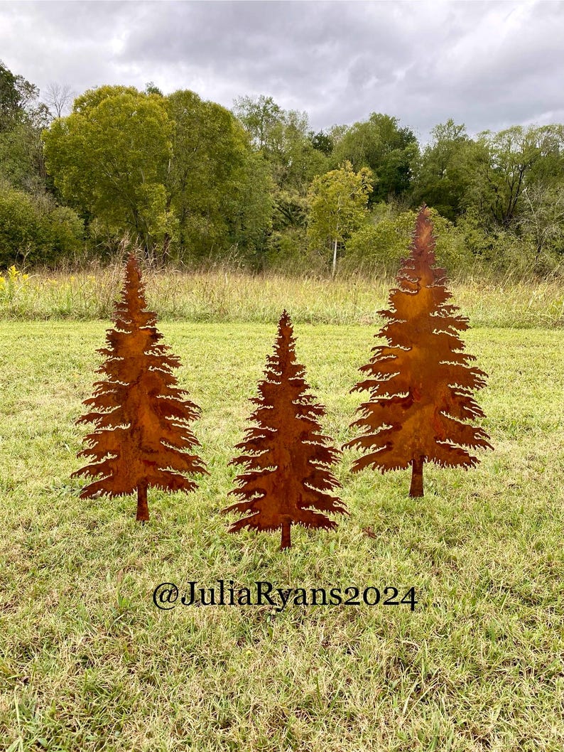 May include: Three rusty metal silhouette trees in a grassy field. The trees are in a row and are all the same size. The trees are a dark brown color and have a rough texture. The trees are in front of a green field and a cloudy sky.