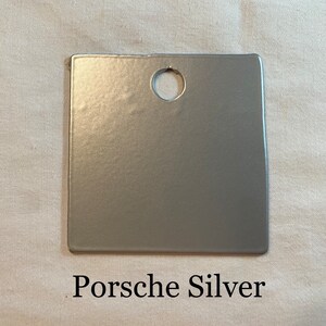 K&ouml;nnte beinhalten: Ein kleiner, quadratischer, silberfarbener Farbmuster mit einem Loch in der Mitte. Der Text "Porsche Silver" ist unter dem Muster aufgedruckt.