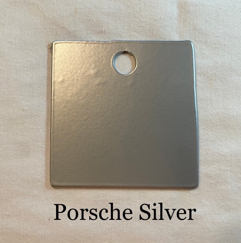 K&ouml;nnte beinhalten: Ein kleiner, quadratischer, silberfarbener Farbmuster mit einem Loch in der Mitte. Der Text "Porsche Silver" ist unter dem Muster aufgedruckt.