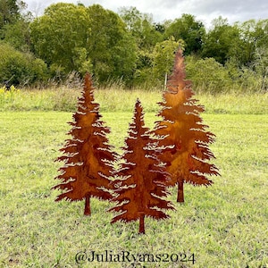 May include: Three rusty metal pine tree silhouettes are displayed on a grassy lawn. The trees are cut out and have a rustic, weathered look. The trees are arranged in a staggered formation, with the tallest tree in the center.