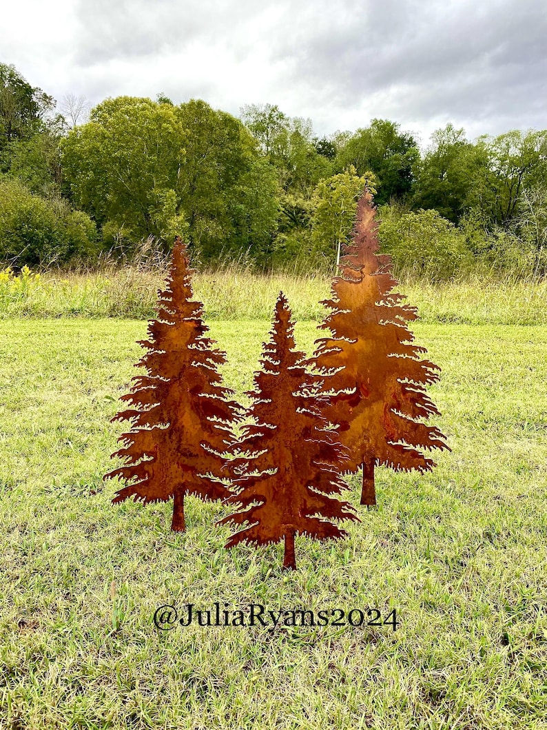 May include: Three rusty metal pine tree silhouettes are displayed on a grassy lawn. The trees are cut out and have a rustic, weathered look. The trees are arranged in a staggered formation, with the tallest tree in the center.