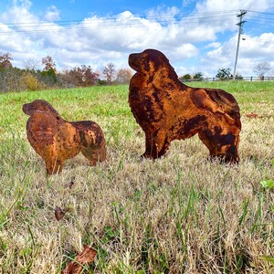 K&ouml;nnte beinhalten: Zwei rostige Metallsilhouetten von Hunden, die auf einer grasbewachsenen Wiese stehen. Der gr&ouml;&szlig;ere Hund steht mit dem Kopf nach links gedreht, w&auml;hrend der kleinere Hund mit dem Kopf nach rechts gedreht steht. Der Himmel ist blau mit wei&szlig;en Wolken.