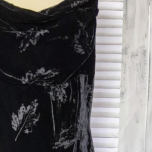 May include: A black velvet dress with a cowl neck and a leaf print. The dress is sleeveless and has a fitted silhouette.