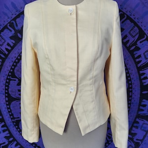 May include: Pale yellow blazer with a round neckline and long sleeves. The blazer has a single-button closure and a tailored fit. The fabric appears to be a lightweight linen or linen blend. The blazer is displayed on a mannequin.