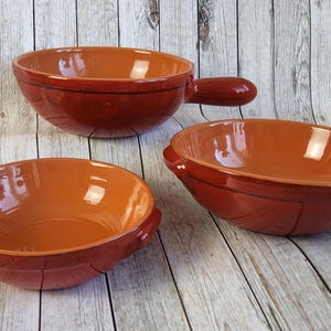 Puede incluir: Una taza de cerámica blanca con un asa negra y el texto "But First, Coffee" en un estilo manuscrito. La taza está sobre una superficie blanca. La taza mide aproximadamente 10 cm de alto.