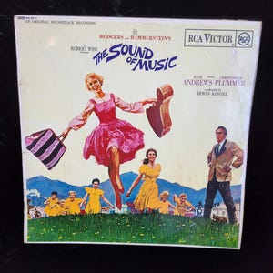 Pode incluir: Capa de álbum de vinil vintage de "The Sound of Music". A capa apresenta uma mulher com um vestido rosa, segurando um estojo de guitarra e uma bolsa listrada, com outros personagens em vestidos e ternos amarelos. O logotipo da RCA Victor é visível.