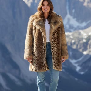 May include: A leopard print faux fur coat with a wide collar and long sleeves. The person is wearing blue jeans and white trainers. The background features a mountain range.