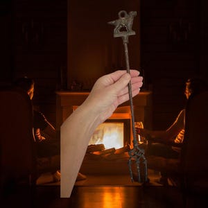Könnte beinhalten: Ein antiker Kamin-Schürhaken aus dunklem Metall. Der Schürhaken hat eine Hundesilhouette an der Spitze, einen langen Griff und eine dreizackige Gabel am unteren Ende. Die Hundesilhouette ist auf einem dekorativen Sockel angebracht.