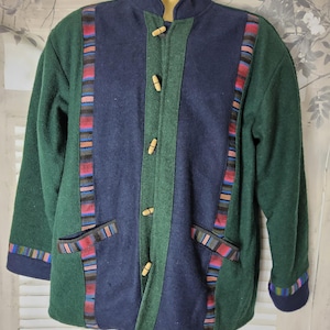 Peut inclure: Veste verte, marine et bleue avec un col montant et des fermetures à bascule en bois. La veste présente des accents rayés colorés sur le devant, les poches et les poignets. La veste est faite d'une matière épaisse et chaude.