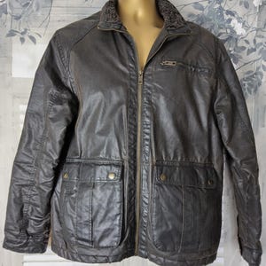 Puede incluir: Una chaqueta de algodón encerado marrón con cuello forrado de forro polar, cierre de cremallera y dos bolsillos grandes con solapa y cierre de botón.