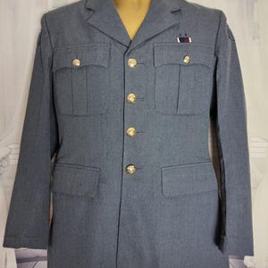 May include: A gray wool blazer with gold buttons and a small patch on the lapel. The blazer has two flap pockets and a single button closure.