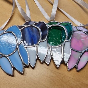 May include: Five stained glass ornaments in various colors, including blue, purple, green, and pink, with silver trim. Each ornament is attached to a white ribbon.