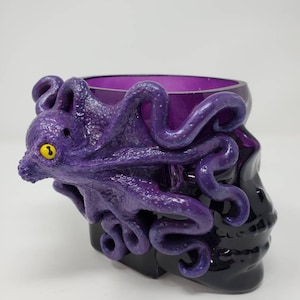 May include: Purple glass skull with a purple octopus wrapped around it. The octopus has a yellow eye.
