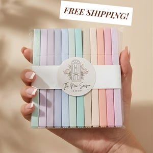 以下が含まれることがあります： ミント、ラベンダー、ライトブルー、クリーム、ピーチ、ピンクのパステルカラーの長方形のペン10本セット。透明なプラスチック製のスリーブに入っており、中央には「The New Season SHOP」と書かれた円形のロゴが入った白い紙の帯が巻かれています。