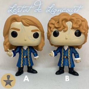 May include: Two vinyl figures of Lestat de Lioncourt, each featuring light brown hair, pale skin with blue vein details, and a blue coat with gold trim. Figure A has straight hair, while Figure B has curly hair. Both figures wear black boots.