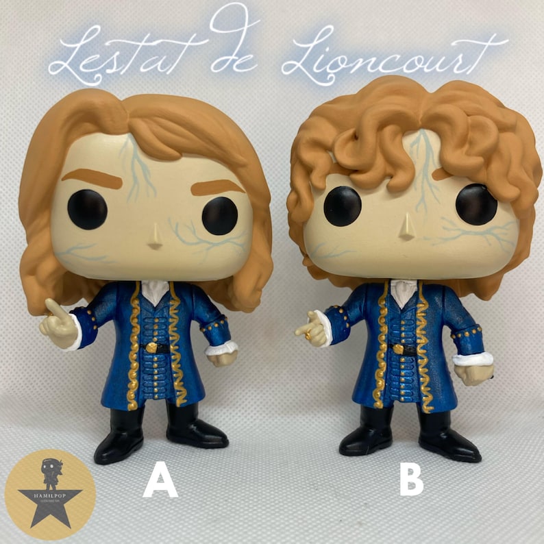 May include: Two vinyl figures of Lestat de Lioncourt, each featuring light brown hair, pale skin with blue vein details, and a blue coat with gold trim. Figure A has straight hair, while Figure B has curly hair. Both figures wear black boots.