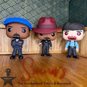 Puede incluir: Tres figuras de Funko Pop: una con gorra azul y traje, otra con sombrero fedora burdeos y traje, y otra con camisa azul claro y tirantes. La palabra "Sinners" está escrita en guion rojo. El texto "The Smokestack Twins & Remmick" está debajo.