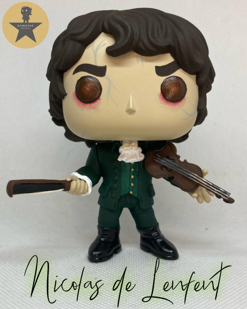 May include: A stylized vinyl figure of a character with dark brown hair, wearing a dark green coat with gold buttons, a white cravat, and black boots. The figure holds a brown violin and a bow. The text "Hamilpop" appears in a circle, and "Nicolas de Lenfent" is written below.