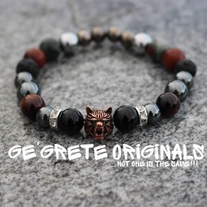 May include: A black and red beaded bracelet with a silver wolf charm. The bracelet is made with lava rock, hematite, and tiger's eye beads. The wolf charm has green eyes and is made of metal.