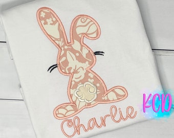 May include: A white t-shirt with a pink floral bunny applique and the name "Charlie" embroidered in pink thread.