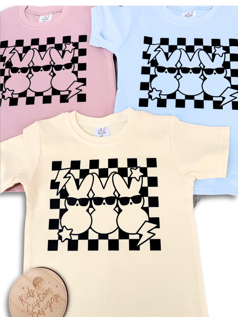 May include: Three pastel coloured t-shirts with a black and white chequered pattern and three cartoon bunnies wearing sunglasses. The bunnies are wearing sunglasses and have a lightning bolt and star design.