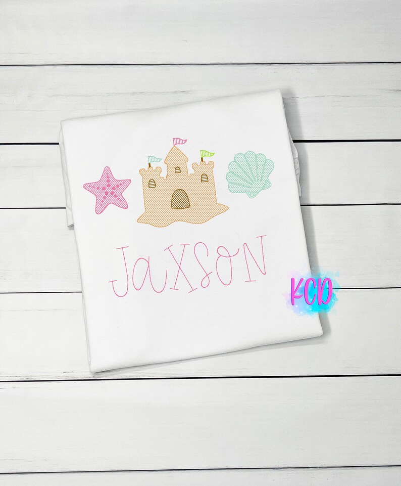 May include: A white t-shirt with a pink sandcastle, a pink starfish, a green seashell, and the name "Jaxson" embroidered in pink.