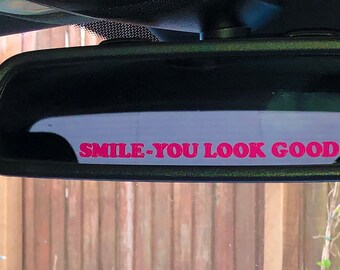 May include: A rearview mirror with a pink sticker that says "SMILE. YOU LOOK GOOD."