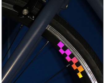 May include: A close-up of a bicycle wheel with a pink and orange reflective stripe. The wheel is black with silver spokes and a silver rim.