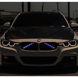 May include: A white BMW with a black hood and blue LED lights in the front grille.
