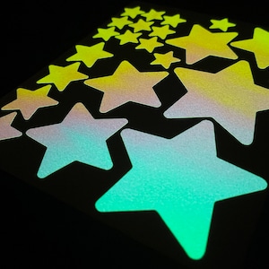 May include: A sheet of glow-in-the-dark star stickers in various shades of green, yellow, and blue. The stars are arranged in a random pattern on a black background.