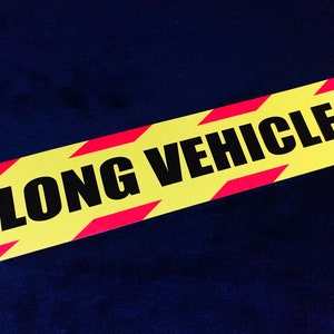Puede incluir: Una señal amarilla y roja a rayas con el texto "LONG VEHICLE" en letras negras.