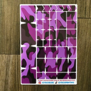 Puede incluir: Una hoja de pegatinas de camuflaje de color morado y negro para personalizar un teclado. Las pegatinas est&aacute;n dispuestas en forma de cuadr&iacute;cula e incluyen teclas de flecha. El texto en la parte inferior dice "WE PRINT CUSTOM STICKERS EMAIL US: HELLO@THEJOYBOX.CO.UK JOYBOXBUDE JOYBOXPRINTING".