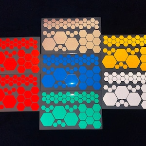 Op de afbeelding: Assortiment van acht vellen met reflecterende zeshoekige stickers in verschillende kleuren, waaronder oranje, rood, blauw, turquoise, geel, wit en beige.