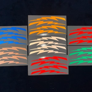 Peut inclure: Ensemble de huit autocollants en vinyle avec un motif d'éclair dans différentes couleurs, notamment orange, rouge, vert, bleu et blanc.