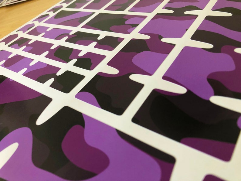Puede incluir: Hoja de pegatinas para teclado de camuflaje morado y negro con recortes blancos para cada tecla.